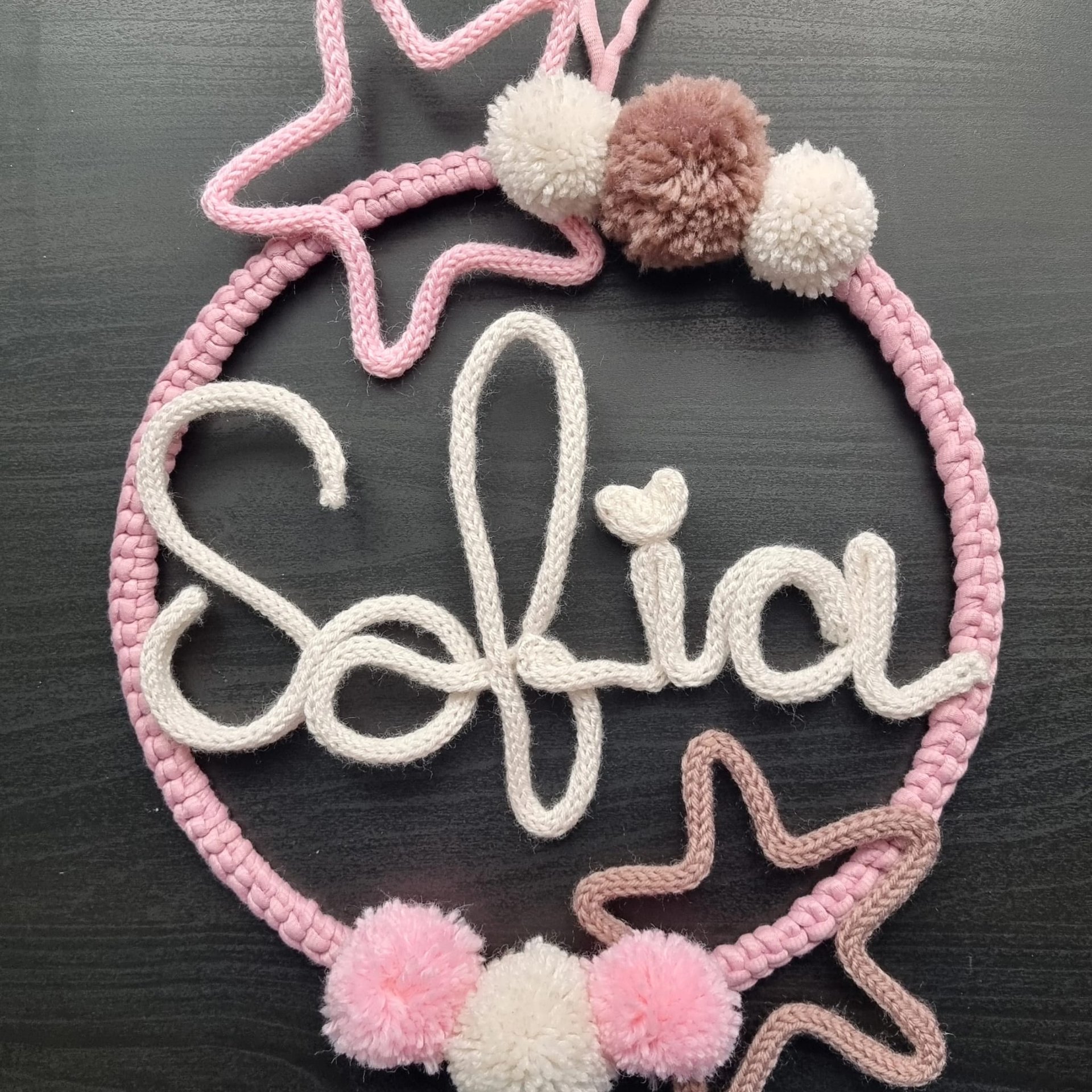 Cerchio in lana rosa con nome Sofia in tricotin panna, stelle rosa e malva e pompon su fondo scuro, Il Mondo di Jessica